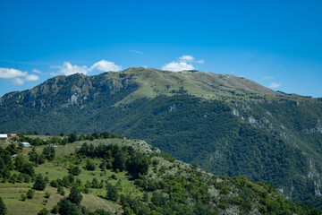 A fragment of a mountain range overgrown with green bushes and grass, a view against the background of a blue cloudy sky. Montenegro