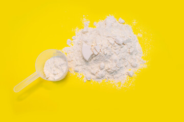 Heap of protein powder with plastic spoon on yellow background