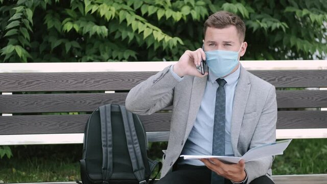Freelancer. The man in disposable mask read the papers sitting on a bench in a city park. Coronavirus. Social distane.