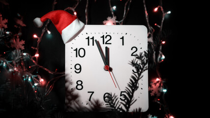 Clock in branches of New Year's fir on black background. Second hand moves in circle of mechanical clock and show Twelve o'clock at  Midnight and the eve of Christmas. Garlands are lit. Festive mood. 