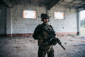 Military man with assault rifle standing inside building, he is ready for combat
