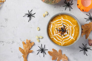 Halloween pumpkin soup with creamy spider web in gray bowl and spiders on the table. View from above. Copy space.