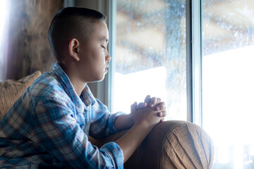 Boy praying on sofa at home, Religion concept.