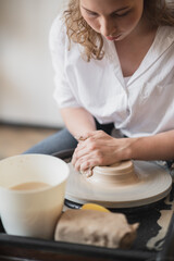 Close-up view of woman hands working on pottery wheel and making clay pot. Hands sculpts a cup from clay pot. Workshop on modeling on the potter's wheel