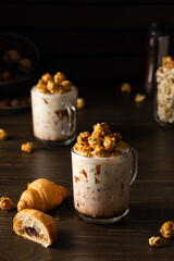 Glass mugs with chocolate milkshake and caramel popcorn and chocolate croissants on wooden...