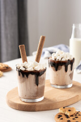 Milkshake with ice cream, marshmallows and chocolate, a glass with a milkshake on a wooden board, chocolate chip cookies and a bottle of milk
