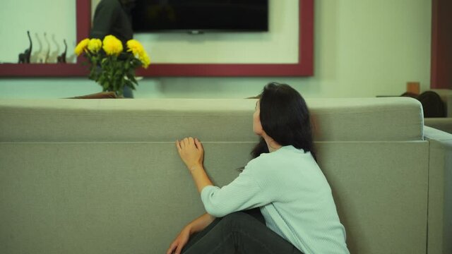 A young girl is hiding from the killer of a maniac with a knife behind the sofa, looking in horror where he is going. 4k