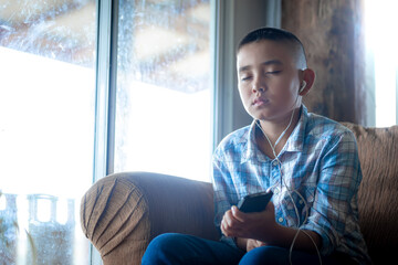 Boy holding phone and listening sermon in mornong on sofa at home, religion concept.