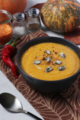 Vegetarian autumn creamy pumpkin soup with red lentils on dark plate. Closeup.