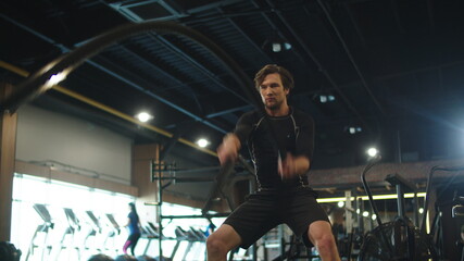 Obraz na płótnie Canvas Focused bodybuilder using battle ropes in sport club. Athlete exercising at gym