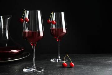 Delicious cherry wine with ripe juicy berries on grey table against black background. Space for text