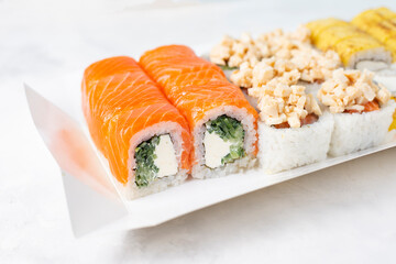 Food delivery, takeaway concept. Lunch box with sushi set. Assorted sushi, Philadelphia roll, cheese, with squid on white light background. Close up. Tasty vegetarian lunch, Japanese cuisine seafood