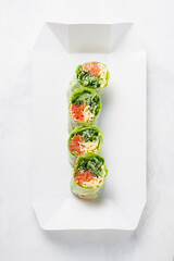 Food delivery, takeaway concept. Lunch box with bright spring roll in rice paper with salmon and herbs, vegetarian lunch. Japanese foo on light background. Japanese cuisine seafood
