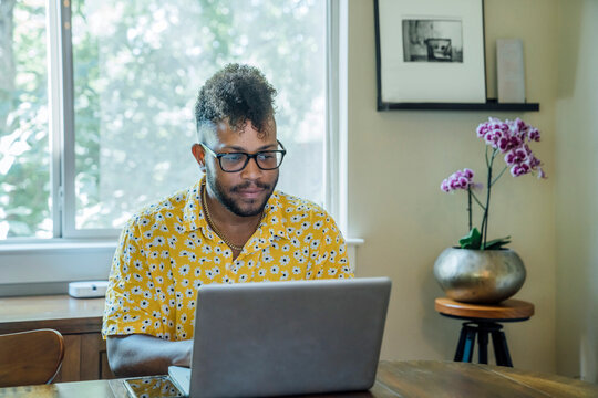 Man Working From Home On Laptop Computer Sitting At Dining Room Table