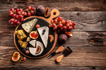 Delicious gourmet cheese, assortment of soft cheeses served with sliced sweet fresh figs and grapes on a rustic wooden background, catering, banner, menu, recipe, place for text