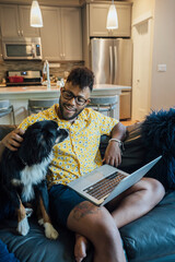 Man working from home with laptop sitting on couch and petting happy Australian Shepherd pet dog
