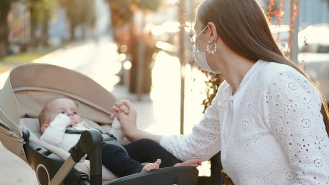 Business woman on maternity leave. Young woman in romantic dress is outside in a city with her baby son in a stroller. The busy mother is sitting on a bench reading documents and looking at her son