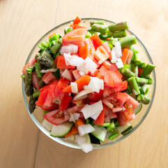 Transparent bowl full of healthy and fresh vegetables on wooden background