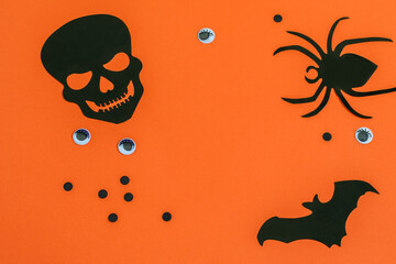 Black decorative skull, spider and bat on the paper orange background. Nice base Halloween flat lay photo.