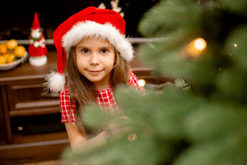Cute little girl in red dress dresses up christmas tree at home