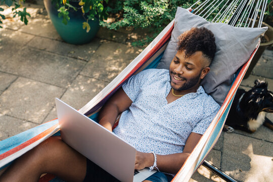 Man Relaxing In Hammock Working On Laptop Computer 