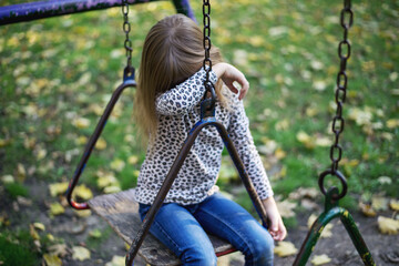 Upset  sad child girl in stress cries at swing rocker
