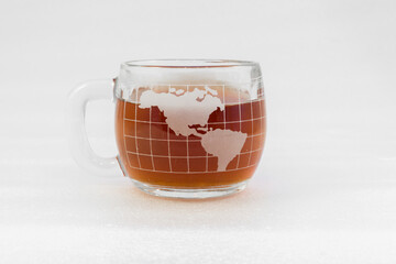 Clear glass coffee cup in shape of a globe filled with coffee with a white background
