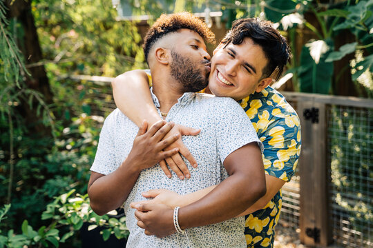 Black man hugging and kissing latinx boyfriend in garden