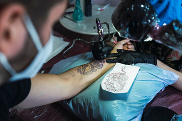 Chica joven con gafas tatuando a chico joven un dragon en el brazo