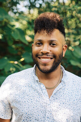 Portrait of smiling, happy confident black man with mohawk standing outdoors in garden