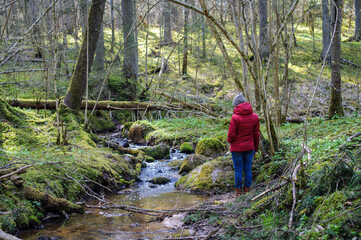 Woman in red jacket is staying near water small stream. Latvia
