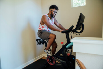 Man working out at home on stationary bike to cycling class on monitor screen