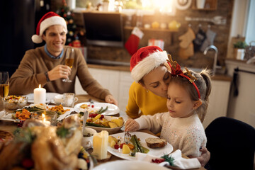 Loving mother kissing her daughter while having family lunch at dining table on Christmas day.