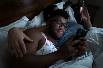 Gay male couple laying in bed together playing on their phones 