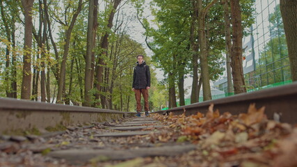 A handsome young man of 18 years in modern warm clothes with a backpack on his shoulders walks on the track, the camera is out of focus. The concept of adolescent loneliness, one in the whole world