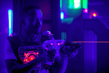 laser tag player holding gun shooting light in black light labyrinth - obrazy, fototapety, plakaty