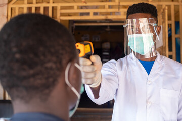 man in full protective medical gear from coronavirus using an infrared thermometer to test a man in...