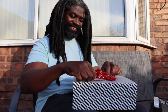 Man Smiling As He Secretly Wraps Gift Box For Family Outside At Home