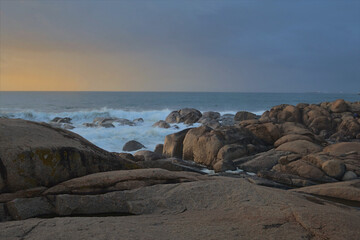 Atlantic coast at sunset.
Golden sunlight illuminates the coastline of stones. The ocean and sky in the background are blue and gold.
