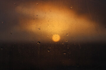Sun at sunset after rain. View behind glass with large raindrops.