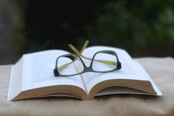 Open book and reading glasses in a garden. Selective focus.