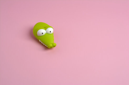 detail of a green plastic crocodile with round white eyes on a smooth pink background