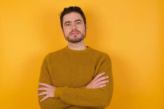 Self Confident Serious Calm Young Man Wearing Casual Sweater And Over Isolated Yellow Background Stands With Arms Folded. Shows Professional Vibe Stands In Assertive Pose.