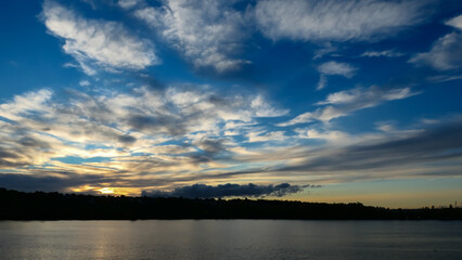Fototapeta premium Amazing sunset over the water. Beautiful landscape with a lake and dramatic sky with cumulus clouds on the horizon. 