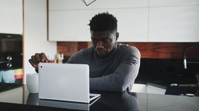 young african american black man working on laptop in his appartment and drinking tea or coffee. High quality 4k footage