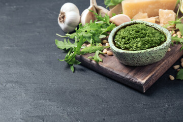 Bowl of tasty arugula pesto and ingredients on black table. Space for text