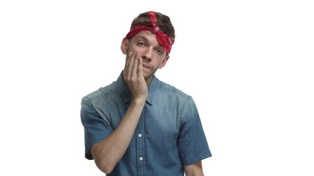 Young exhausted hipster guy with beard, red bandana wrapped over forehead, making facepalm and looking annoyed, standing bothered over white background