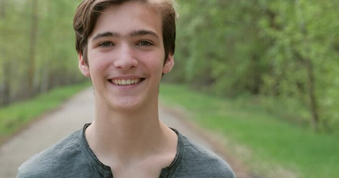 Young happy man looks on the camera in the nature. Smiling young teenager, outdoors. Closeup face of  handsome cheerful guy, on the nature. 