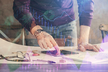 Double exposure of man's hands holding and using a digital device and forex graph drawing....