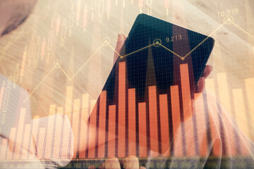 Double exposure of man's hands holding and using a digital device and forex graph drawing. Financial market concept.